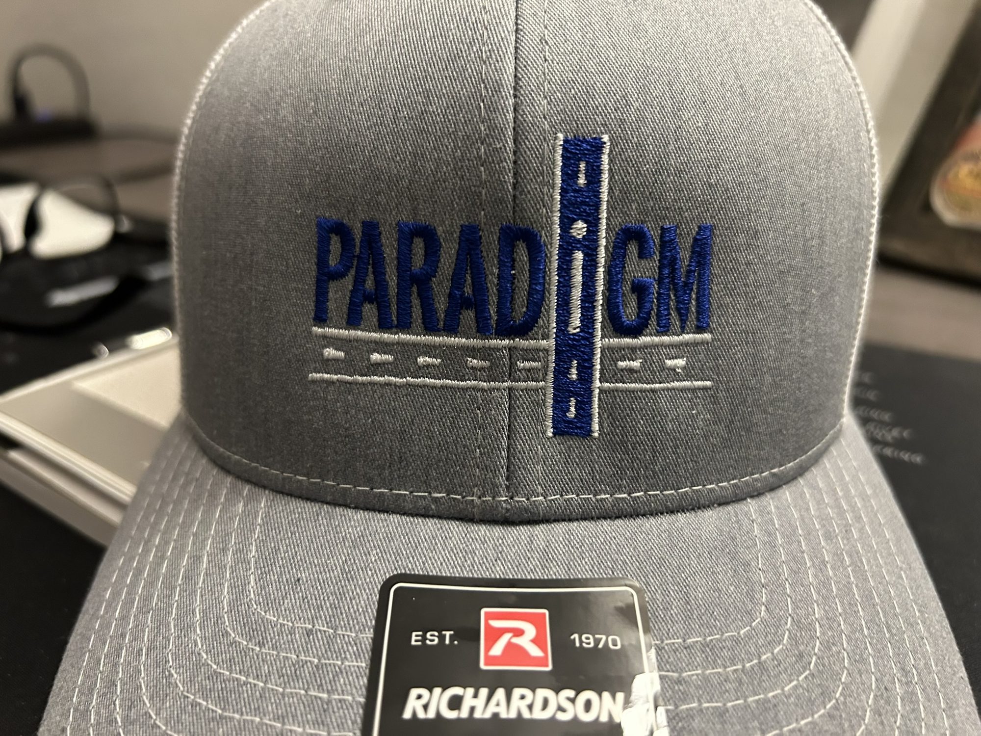 Grey Richardson trucker hat with embroidered Paradigm road-mark logo